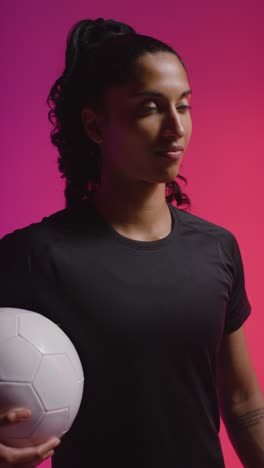 Vertical-Video-Studio-Portrait-Of-Woman-Wearing-Sports-Clothing-Holding-Ball-Against-Coloured-Background